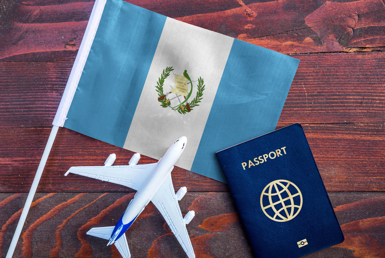 Flag of Guatemala with passport and toy airplane on wooden background.